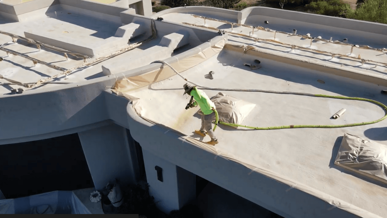 HailCo Roofing crew member applying new spray polyurethane foam across a wide low-slope section of the Desert Highlands estate roof