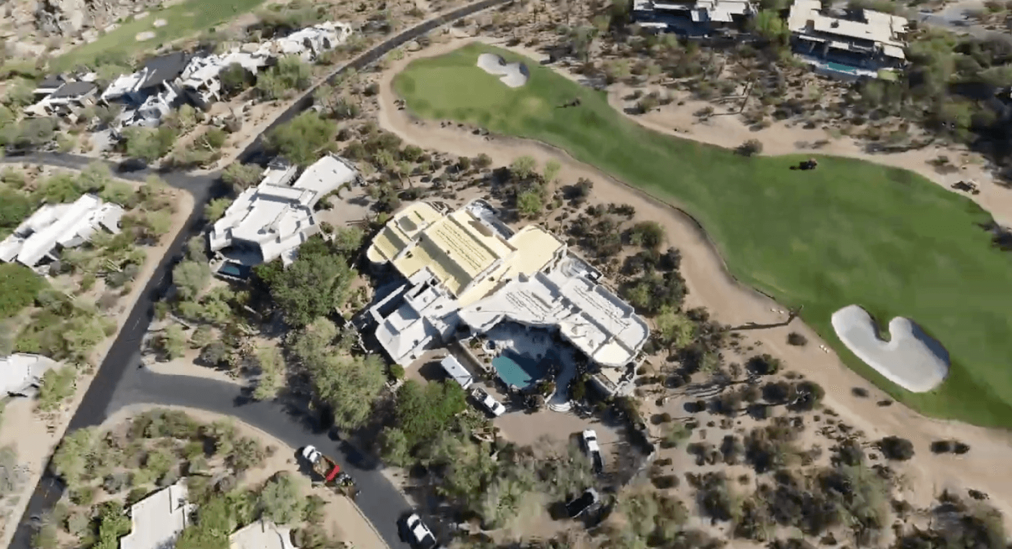 Drone view of a Desert Highlands estate mid-project, fresh spray foam being applied across the roof with the golf course greens and bunkers beyond